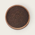 Top view of a round wooden container filled with loose black tea leaves, centered on a white background.