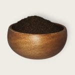 A wooden bowl filled with black tea leaves, isolated on a white background.